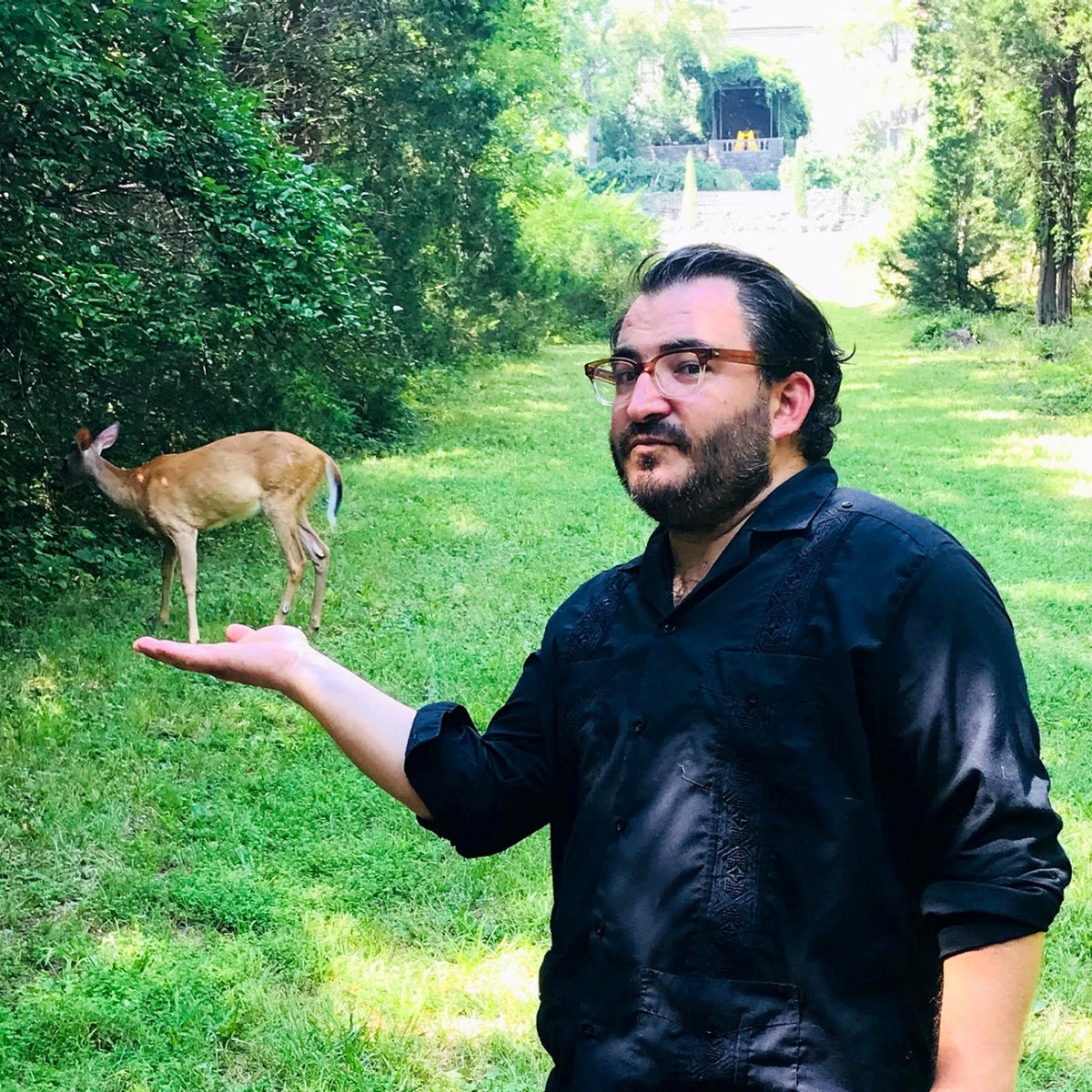 A photo of David foregrounding a deer with his palm out appearing to be holding a the deer.